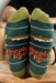 Green fishing socks with 'Keeping it Reel' text worn by a person sitting on a wooden stool.